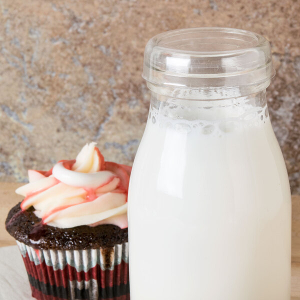 A wooden table with a glass jar of milk and a cupcake with an American Metalcraft round PET milk bottle cover on top.
