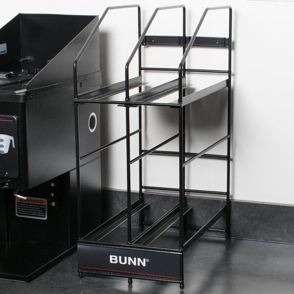 A black metal shelf with 4 black Bunn Smart Hoppers on a black machine.