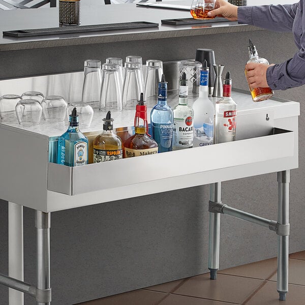 A person using a Regency stainless steel speed rail to pour alcohol into a glass on a bar counter.