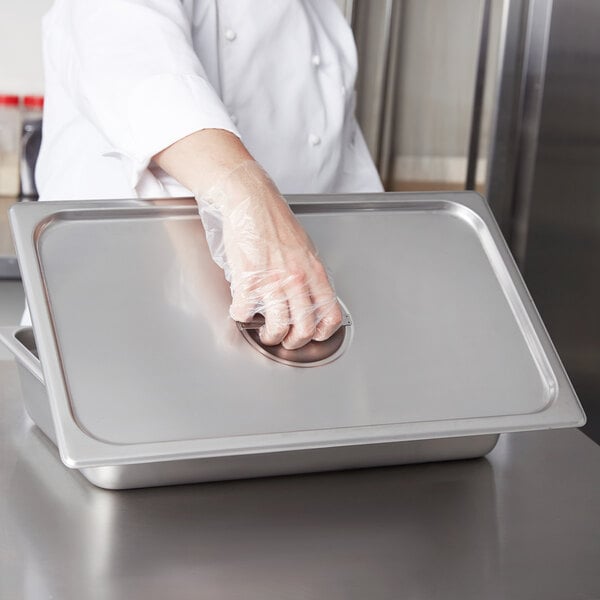 A person wearing a glove holds a stainless steel Choice full size steam table pan cover.