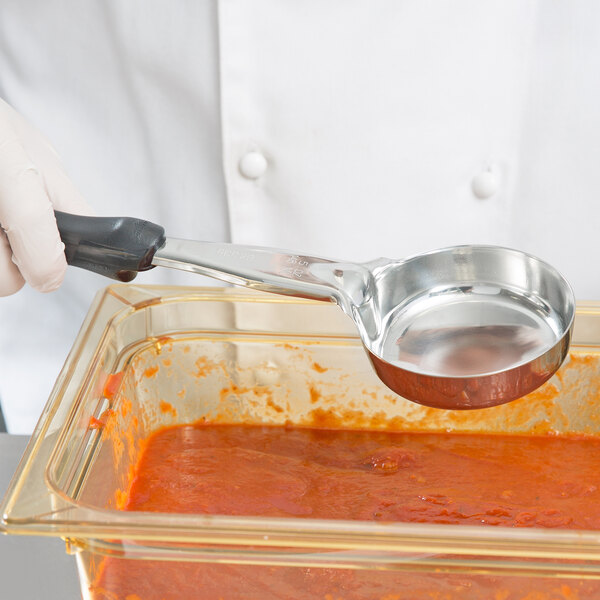 A person in white gloves using a Vollrath black round spoodle to serve red sauce.