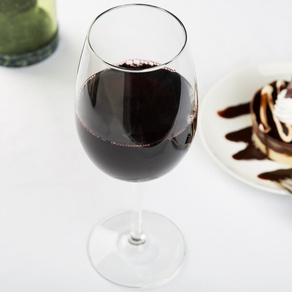 A Libbey wine glass filled with red wine next to a plate of chocolate dessert.