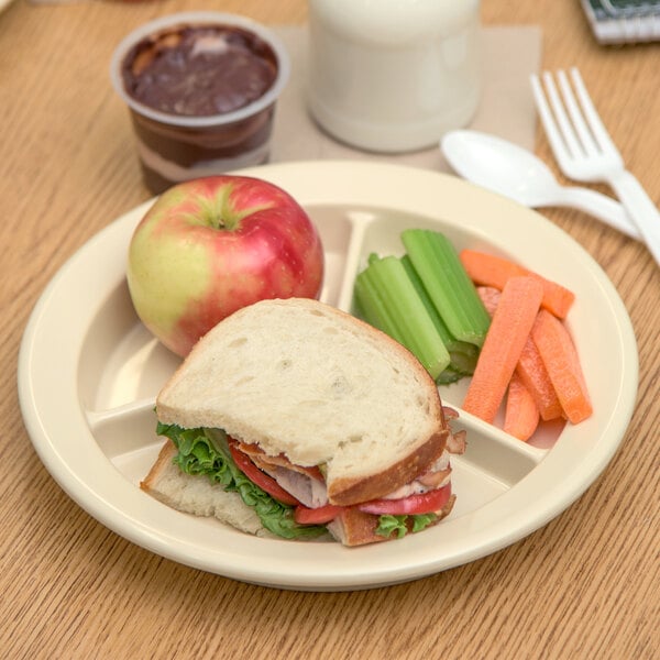 A Carlisle tan melamine plate with a sandwich, carrots, and celery.