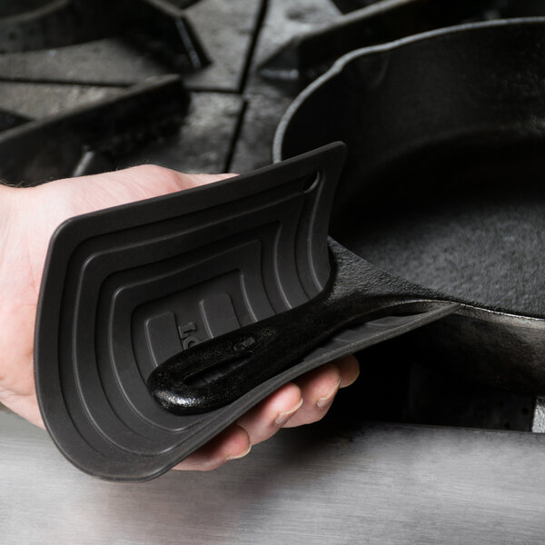 A person using a black Lodge silicone pot holder to hold a black cast iron skillet.