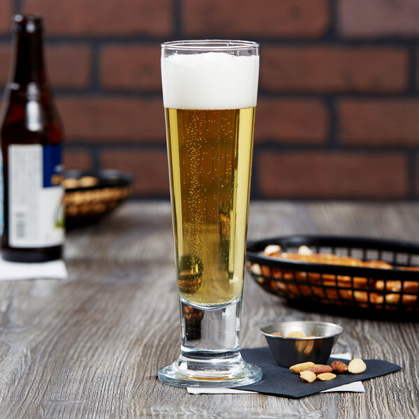 A footed pilsner glass of beer on a table.