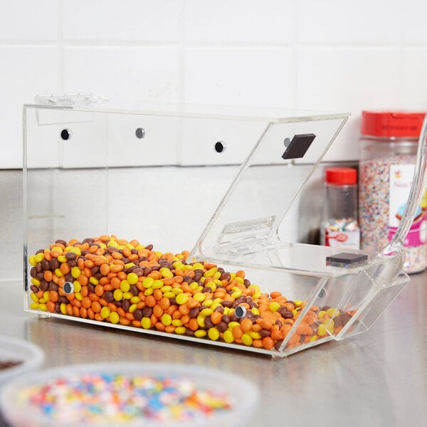 A clear plastic container with a scoop holster holding a container of candy.