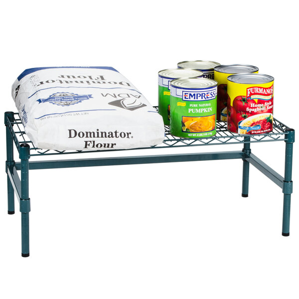 A Regency green wire dunnage rack holding canned and bagged food outdoors.