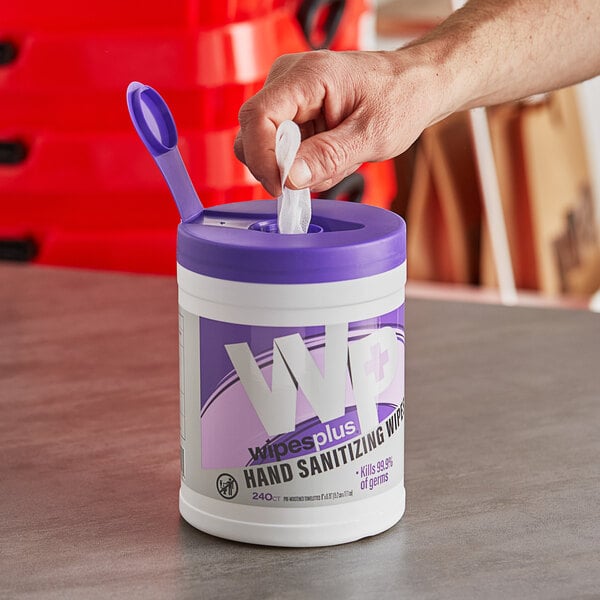 A person's hand using a purple container of WipesPlus hand sanitizing wipes.
