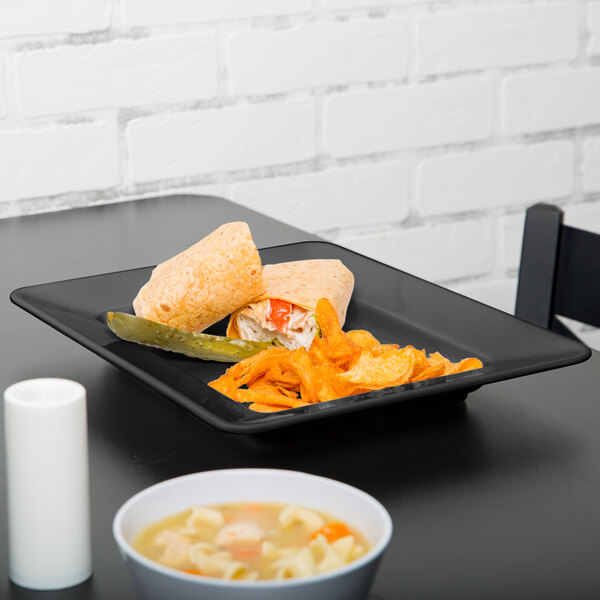A black rectangular Milano plate with a tortilla wrap, soup, and a sandwich on it.