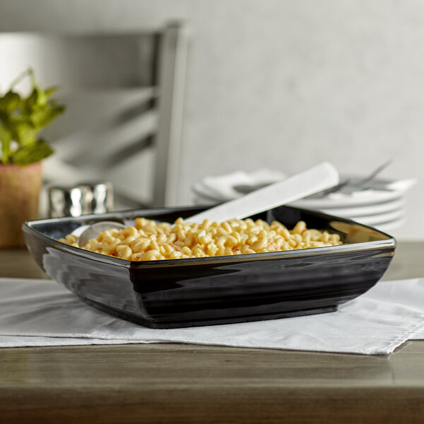 A black rectangular melamine bowl with food on a table.