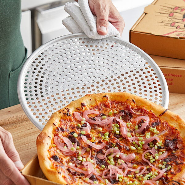 A person using an American Metalcraft 10" Mega Pizza Screen to hold a pizza.