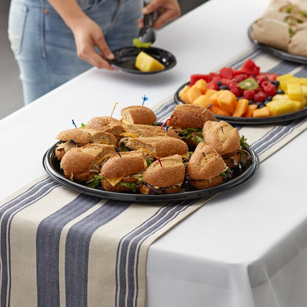 A woman serving sandwiches on a Visions Black catering tray on a table.