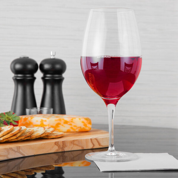 A Stolzle Bordeaux wine glass filled with red wine next to a plate of crackers.