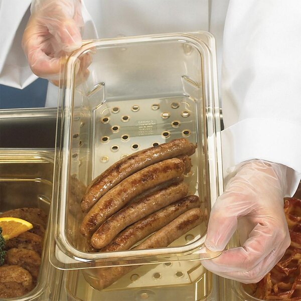 A person wearing a glove using a Cambro amber plastic colander pan to hold sausages.