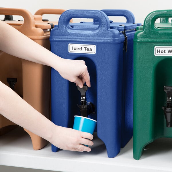 A person filling a blue Cambro insulated beverage dispenser with water.