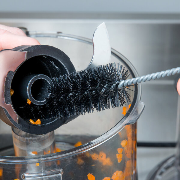 A hand using a Waring cleaning brush with a round black tip to clean a food processor.