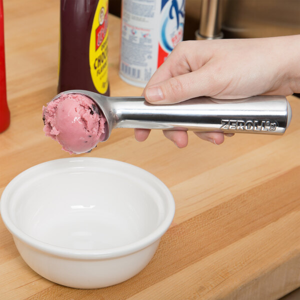 A hand using a Zeroll aluminum ice cream scoop to scoop ice cream into a bowl.