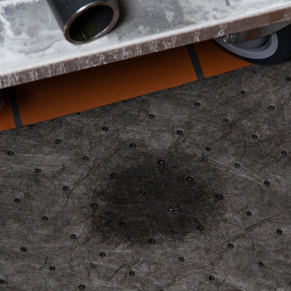 A close-up of a metal grate with a black spot on a grey surface.