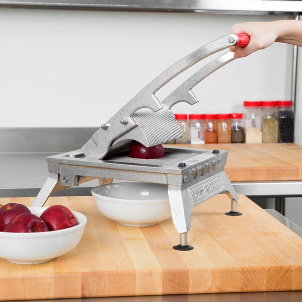 A person using a Vollrath Redco fruit slicer to cut a red apple.