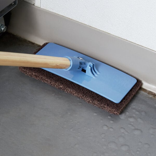 A Scrubble multi-purpose pad holder with a wooden pole cleaning a floor.