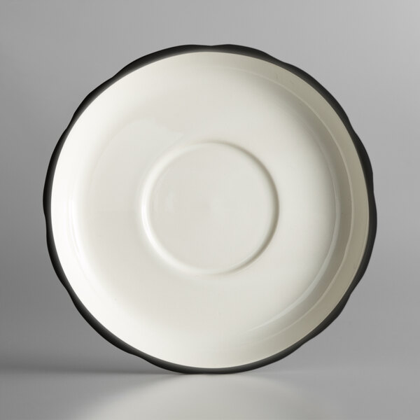 A CAC ivory saucer with a scalloped edge and black rim.