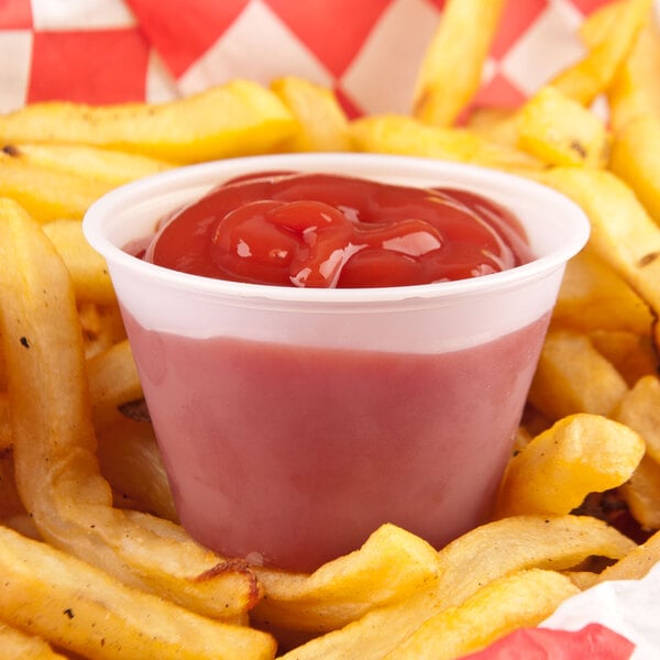 A Solo translucent polystyrene portion cup of ketchup on french fries.