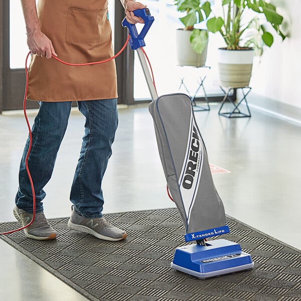 A man using an Oreck upright bagged vacuum cleaner to clean the floor.