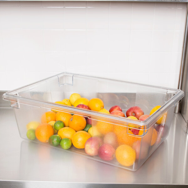 A Rubbermaid clear polycarbonate food storage box filled with fruit including apples and oranges.