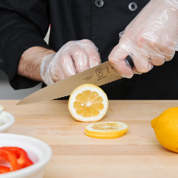 A person using a Mercer Culinary Millennia serrated wavy edge chef knife to cut a lemon on a wooden surface.