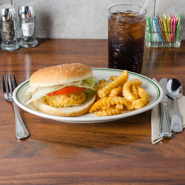 A Homer Laughlin green banded oval platter with a burger, fries, and a soda on a table with a fork.