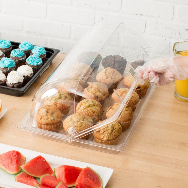 A hand holding a clear plastic tray of muffins and cupcakes with a roll top cover.
