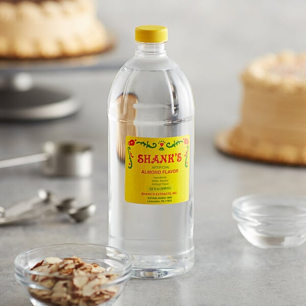 A bottle of Shank's Imitation Almond Extract on a counter next to a cake and other ingredients.