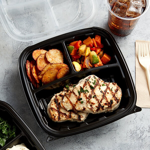 A black plastic 3-compartment hinged container with chicken, mixed vegetables, and a drink.