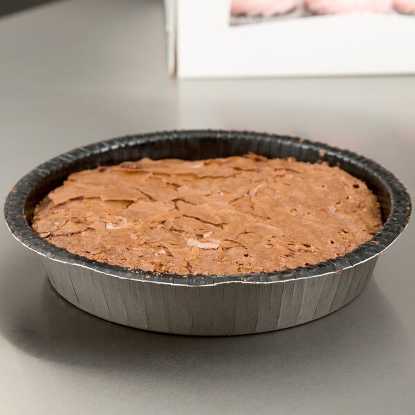 A brown cake in a Solut round paperboard cake pan on a table.