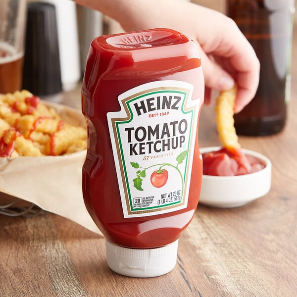 A hand holding a french fry and a Heinz Ketchup bottle on a table.