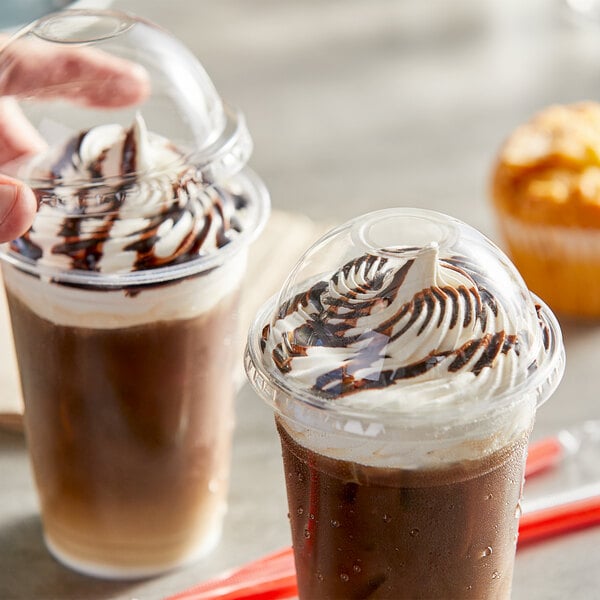 A plastic cup with a Choice clear dome lid and a drink with whipped cream and chocolate in it.