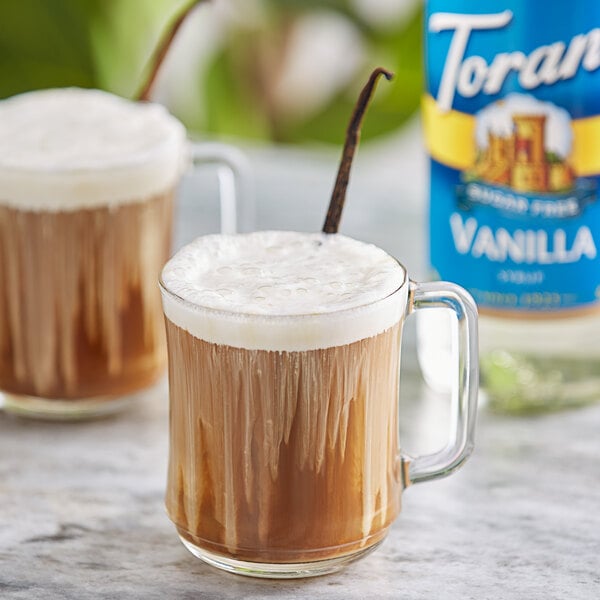 A glass mug of brown liquid flavored with Torani Sugar-Free Vanilla Syrup and a vanilla stick.