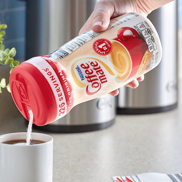 A hand pouring Nestle Coffee-Mate Original coffee creamer into a cup of coffee.