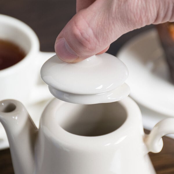 A person's finger pressing a white Homer Laughlin lid on a white teapot.
