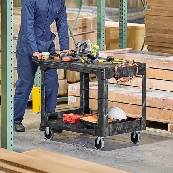 A man standing next to a black Rubbermaid utility cart with tools on it.