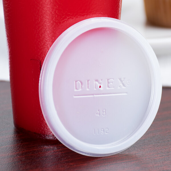A white plastic lid for a Dinex juice cup sitting on a table.