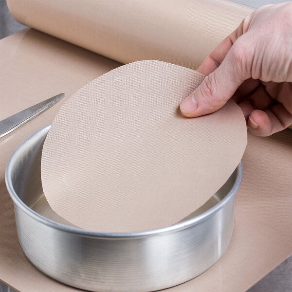 A hand using a knife to cut a circular pan liner in a metal pan.