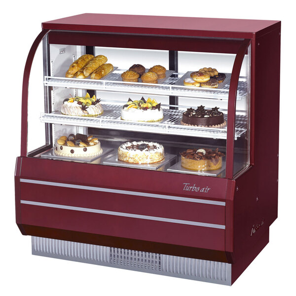 A red Turbo Air curved glass dry bakery display case with cakes and pastries inside.