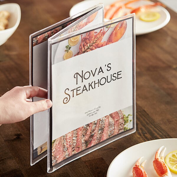 A hand holding a menu with a clear menu cover on a table.