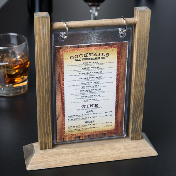 A Menu Solutions antiqued wood table tent with a plastic sheet displaying a menu on a table in a cocktail bar.