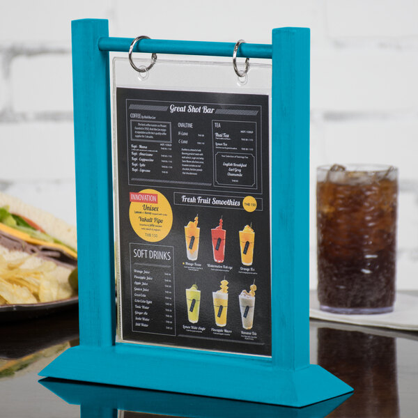 A Menu Solutions sky blue wood flip top table tent on a table with a drink on it.