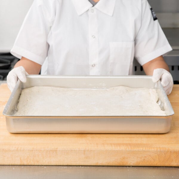 A person in white gloves holding an American Metalcraft aluminum cake pan.