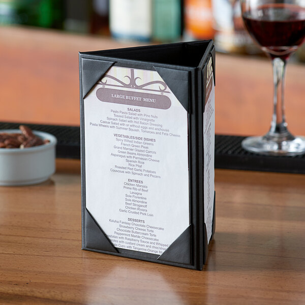 A Menu Solutions triple panel table tent with a menu on a table with a glass of wine.