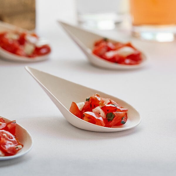 A white table with EcoChoice compostable sugarcane taster spoons filled with food.