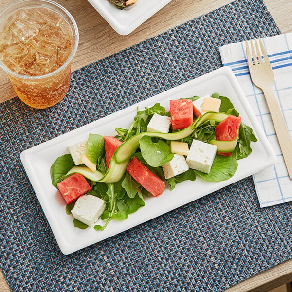 A rectangular EcoChoice bagasse plate with salad, watermelon, and cheese on a table.